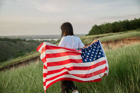 4th of July. Fourth of July. Joyful woman with the national American flag against beautiful landmark. Independence Day. Patriotic holiday, democracy respect and veteran respect conceptの写真素材