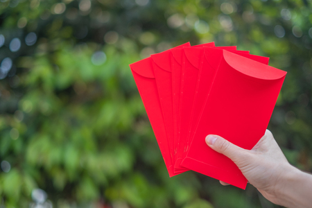 Happy Chinese new year, Hand holding red envelope or called Angpao isolated on green bokeh background from trees.の写真素材
