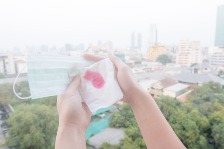 Woman hands or female hands holding a protective mask and napkin with blood because of air pollution in the city have particulate matters or PM 2.5 with city building backgroundの写真素材