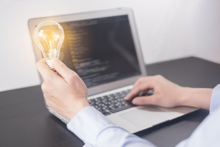 Young woman programmer hand holding light bulb, woman hands coding and programming on screen laptop, new ideas with innovation and creativity conceptの写真素材