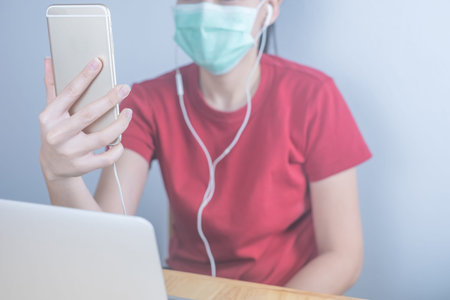 Asian woman wearing hygiene protective mask to protect COVID19, making facetime video calling with...