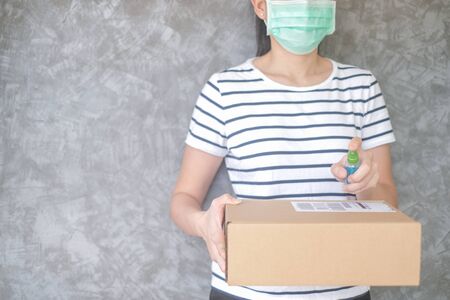 woman wearing protective mask using spray alcohol sanitizer cleaning parcel post to prevent virus and bacterias from Postal sender she protects herself and her family from virus woman giving packageの写真素材