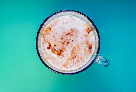 Cup of cappuccino with foam close-up on a blue green background. Coffee in a glass mug, top view, copy space, hot drinkの写真素材