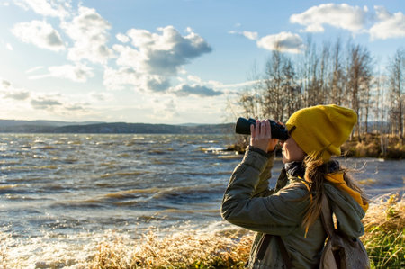 Young woman looking through binoculars at birds on the lake. Birdwatching, zoology, ecology....