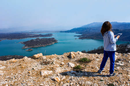 young woman with hair fluttering in the wind takes a photo of the beautiful blue Slansko lake in Montenegro. Scenery. Girl from behindの写真素材
