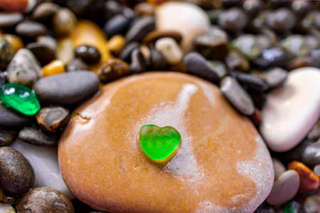 small green heart shaped stone among many pebbles. Natural background, copy space, love, romanceの写真素材