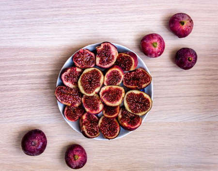 Ripe halves of figs in a plate and whole figs around on a light wooden table close-up. Healthy fresh vegan raw organic foodの写真素材