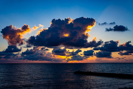 Sunset over the sea, bright sky with large dark clouds and pier