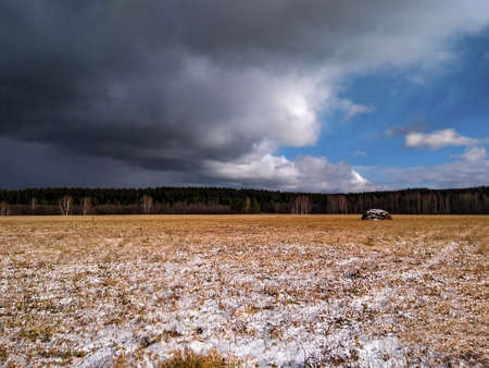 A view of a dry grass field with first snow and a dark cloudy sky. Early winter or late autumn. Sceneryの写真素材