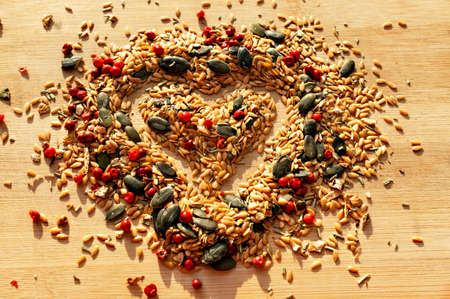 Food background of mix of spices, condiments and seeds close up with selective focus in shape of heart on wooden board, golden flax seeds, pumpkin seeds, red peppers, dried healthy food, mixtureの写真素材