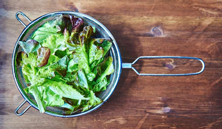 Fresh red and green lettuce with water droplets in a metal colander on a wooden background. Natural organic food. Close-up. Vitamins, diet, vegetarian concept. Healthy vegan eating, small businesの写真素材
