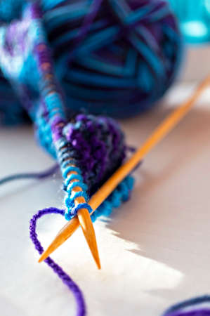 Knitting on wooden knitting needles from violet blue purple yarn close-up on white background. Hobby, homemade, abstract backgroundの写真素材