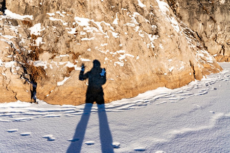 female shadow with long legs and a raised hand on fresh snow and a rock on a winter sunny day. Abstract background, light and shadow, winter funの写真素材
