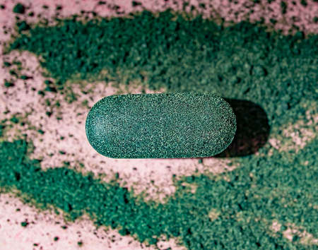 Close-up chlorella or spirulina tablet among the powder on a pink background. Nutritional supplement, detox superfoodの写真素材