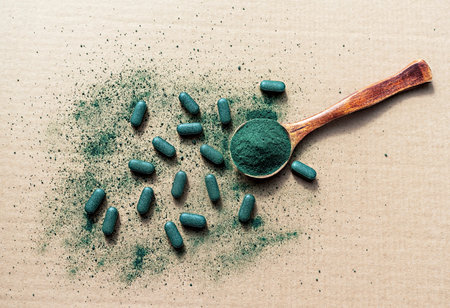 Organic chlorella, spirulina or barley grass powder in wooden spoon and pills on beige paper background. Nutritional supplement, Detox superfood, healthy lifestyleの写真素材