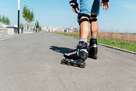 Male legs in roller skates and protective equipment close up riding on the asphalt road in summer, roller-blading, outdoor activity, healthy active lifestyleの写真素材