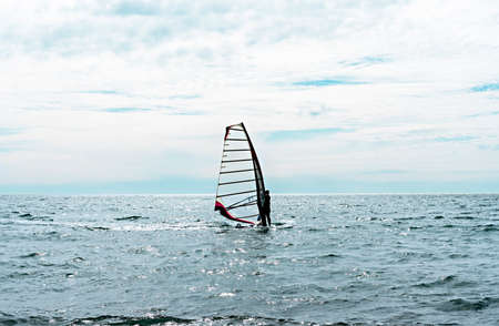 Athlete riding windsurf in the distance on blue sea against blue cloudy sky in summer, water sports, active healthy lifestyle, windsurfing, copy spaceの写真素材