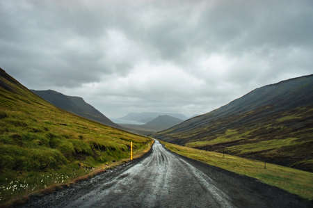 View of wet asphalt road in the green mountains of Iceland and rainy dark sky travel landscape selective focus tripの写真素材