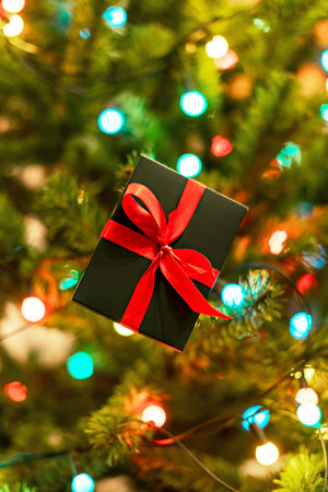 Christmas present on Christmas tree with garland lights , Gift in green box with red ribbon New Year...