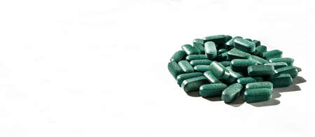 Pills of chlorella, spirulina, barley grass on white background with dark shadows close-up Nutritional supplement, detox superfood copy space health careの写真素材