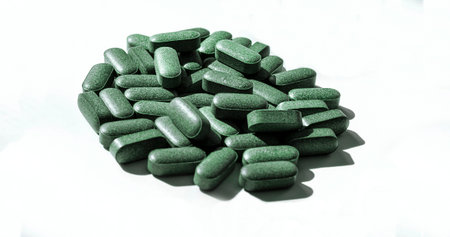 Pills of chlorella, spirulina, barley grass on white background with dark shadows close-up...