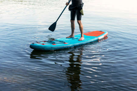 Man faceless in thermo suit paddling stand up paddleboard blue SUP on the water lake with paddle male legs active lifestyle summer activities copy spaceの写真素材