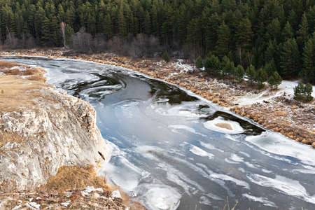 View of river covered with first ice and snow cliffs with dry beige grass and forest in autumn or early winter Landscape earth tonesの写真素材