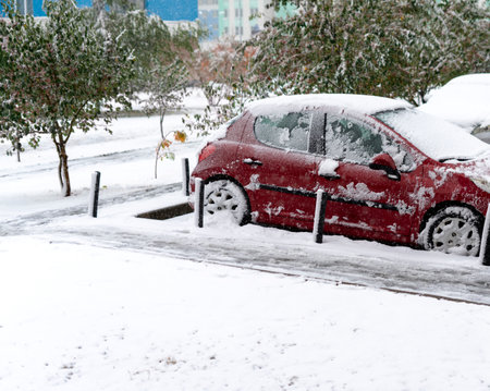 Snowfall on the street and a red car covered with snow winter weatherの写真素材