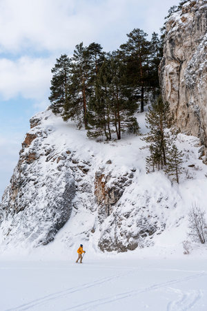 side view of young woman in yellow clothes with backpack skiing near rocks and cliffs Active healthy lifestyle Winter sports Hikingの写真素材