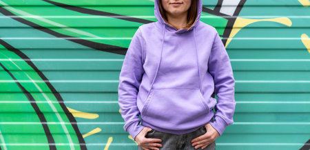Young woman in hood in purple violet hoodie on green modern background copy space mockup friendlyの写真素材