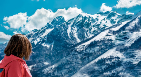 Rear view of young woman in pink hoodie with backpack looking at the view of snowy mountain range...