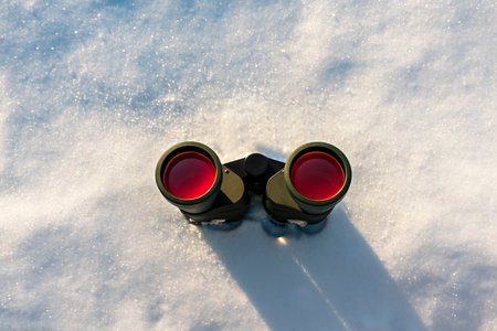 Black binoculars with red lens on white snowy winter background copy space Birdwatching ecology Research in nature, observation of animalsの写真素材