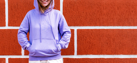 Smiling woman in lilac purple hoodie against red wall background, friendly mockup copy spaceの写真素材