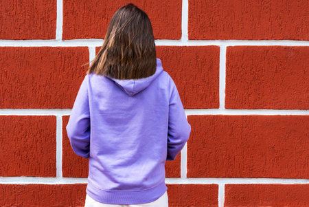 rear view of woman dressed in purple sweatshirt against red wall background , mockup friendly, textile business clothingの写真素材