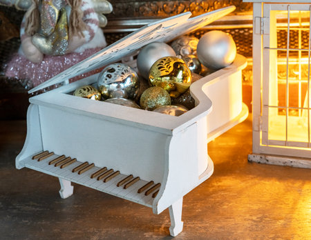 Festive Christmas decorations arranged inside miniature white grand piano, featuring gold and silver ornaments , warm glow of lantern adds cozy holiday atmosphere, seasonal and holiday-themed visualsの写真素材