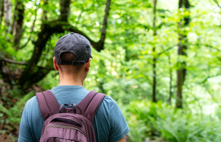 Close-up of hiker walking through lush green forest Man with backpack and cap hiking, outdoor adventure, nature exploration, and solo travel ecotourism Copy spaceの写真素材