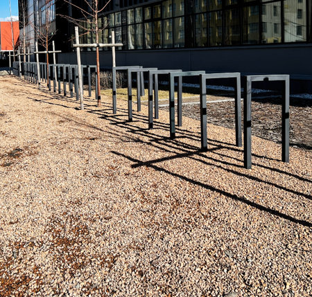 Empty metal bike racks lined up on gravel path outside a modern building, casting distinct shadows...