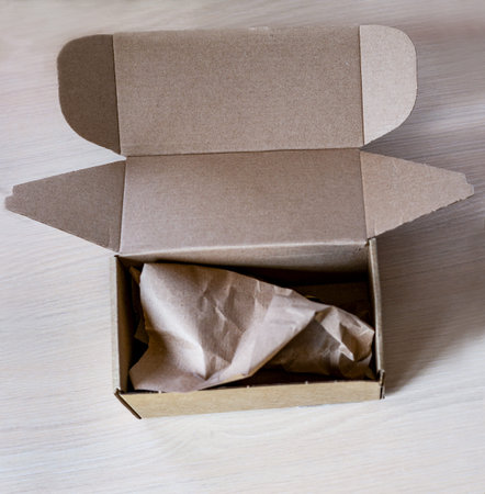 Open kraft cardboard box filled with crumpled brown paper filler on wooden surfaces, eco-friendly...