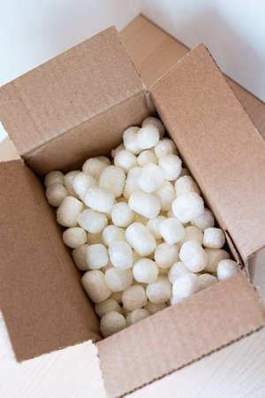 Open cardboard box filled with eco-friendly corn-based packing peanuts on a light wooden surface....
