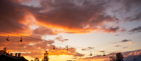Scenic sunset view with vibrant orange and purple clouds, silhouetted ski lift cables, and distant mountains creating a tranquil atmosphere for outdoor enthusiasts and nature loversの写真素材