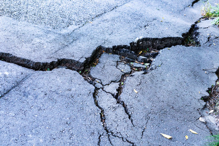 Asphalt road surface shows significant cracks and fissures caused by landslide, highlighting the...