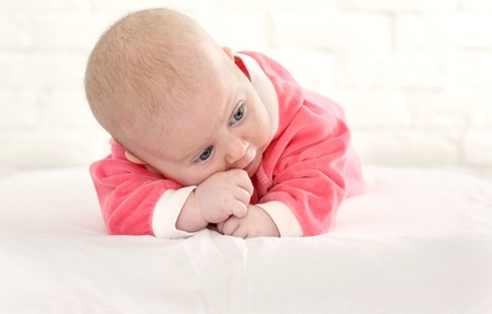 baby in is bright-pink overalls lies on a stomachの写真素材