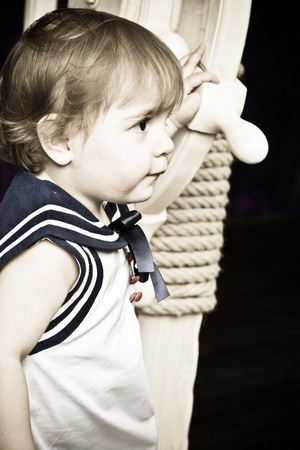 little girl in a dress in sailor's style holds a wooden steering wheel. Studio shooting.の写真素材