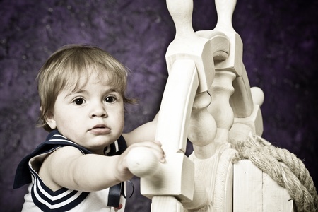 little girl in a dress in sailor's style holds a wooden steering wheel. Studio shooting.の写真素材