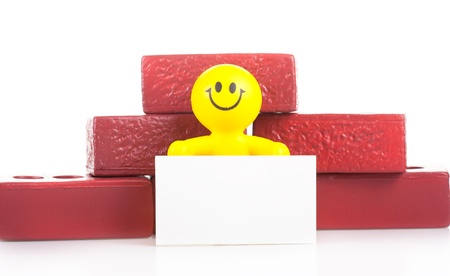 One smiling toy little man near to a heap of bricks holds the pure white form. The building concept.の写真素材