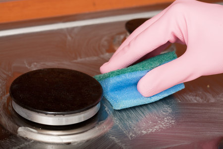hand of the person in a rubber glove cleans a kitchen gas cooker