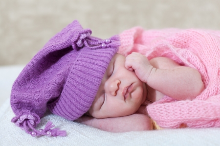  newborn girl in a violet hat sleeps under a pink capeの写真素材