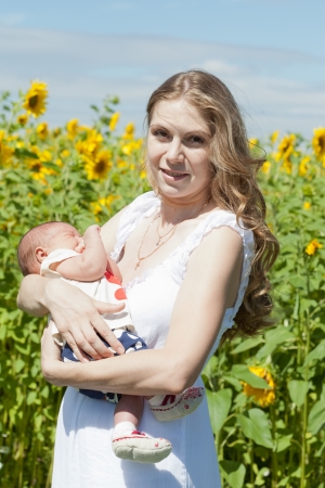 Young mother with the baby among blossoming sunflowersの写真素材