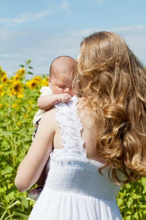 Young mother with the baby among blossoming sunflowersの写真素材