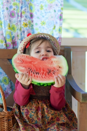  little girl in a straw hat with appetite eats a ripe water-melonの写真素材